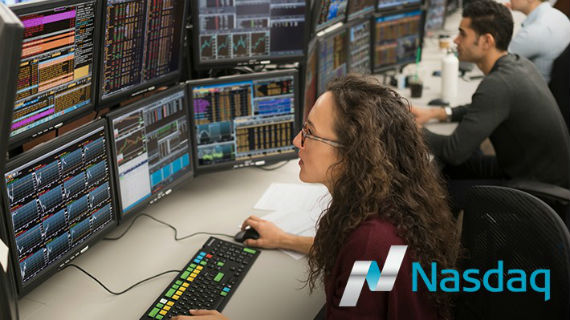 Woman sitting and viewing data on multiple screens, Nasdaq logo in lower right corner
